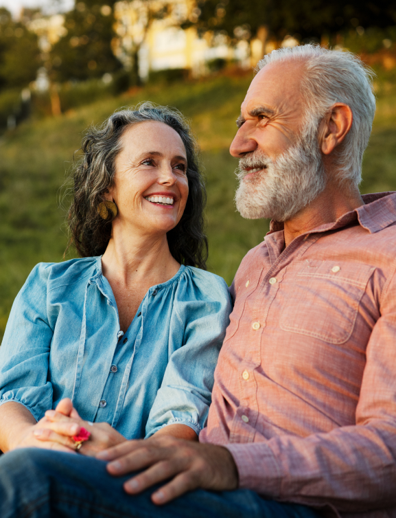 Smiling male and female older adult couple seated in park setting, appearing to enjoy a pause in conversation